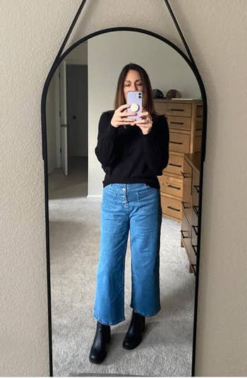 Person in a mirror selfie wearing a black top 
 and high waisted blue wide-leg jeans 