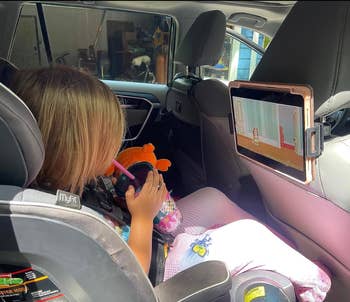 child in carseat watching Bluey on an iPad mounted on the back of a seat 