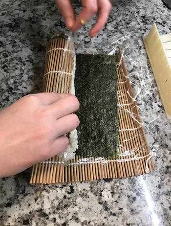 reviewer demonstrating how they use the mat to roll the sushi up