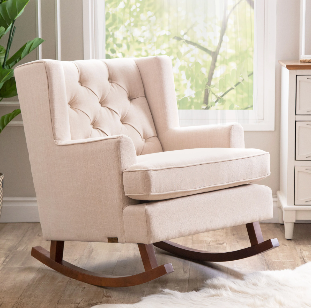 Cream plush arm chair rocking chair with a tufted backing and dark brown wooden gliders on hardwood floor