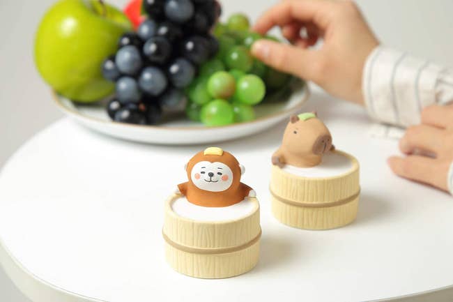 figurines of monkey and capybara sitting in barrels 