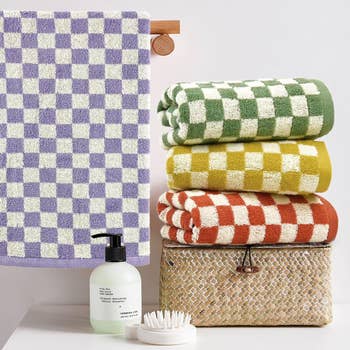 Stacked checkered towels in purple, green, yellow, and red on woven basket next to toiletries