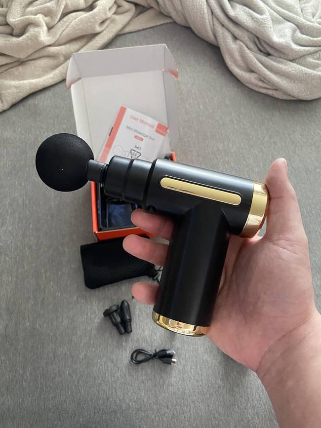 Hand holding a achromatic and golden massage gun