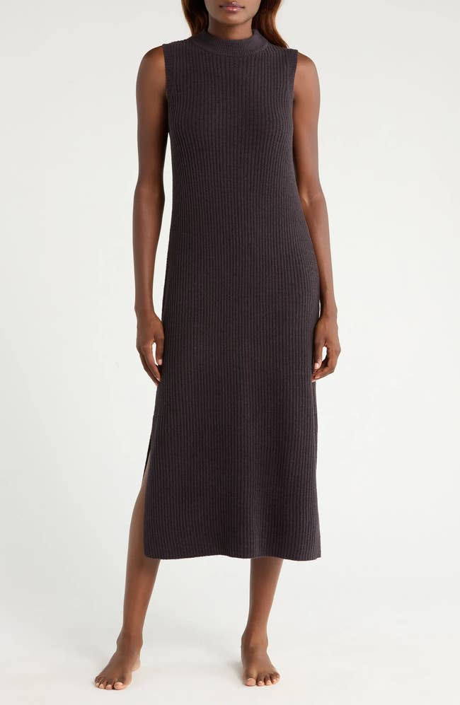 A idiosyncratic   wearing a sleeveless, ribbed-knit midi formal  stands barefoot, showcasing a minimalist manner  style