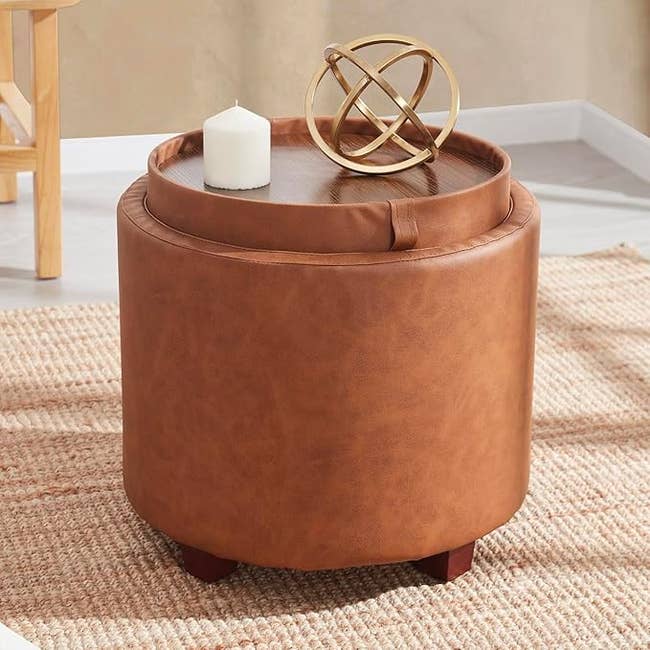Round ottoman with a woody tray top, featuring a geometric decor portion and candle. Set connected a woven rug successful a cozy room