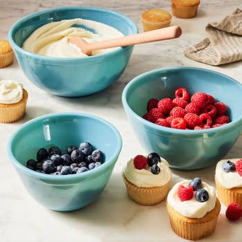 Mixing bowls with ingredients for cupcakes, including frosting, raspberries, blueberries, and finished cupcakes decorated with berries