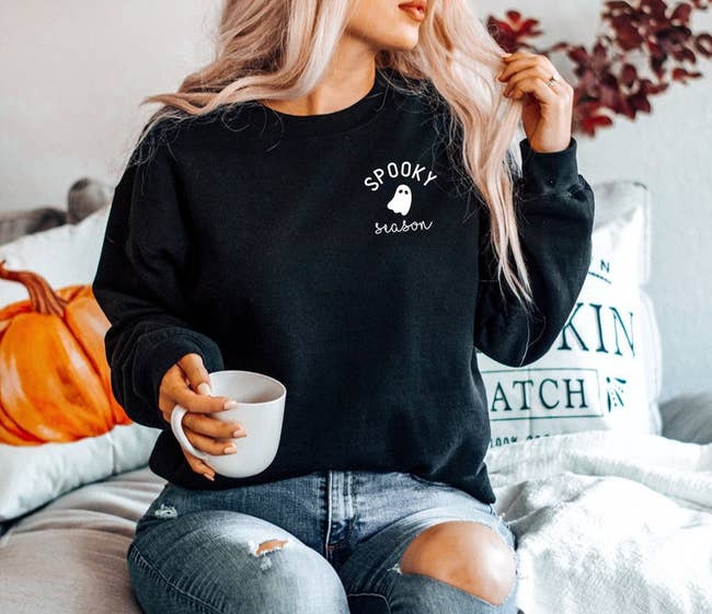 a model wearing a black crewneck sweatshirt with a small ghost print on the chest and text reading 