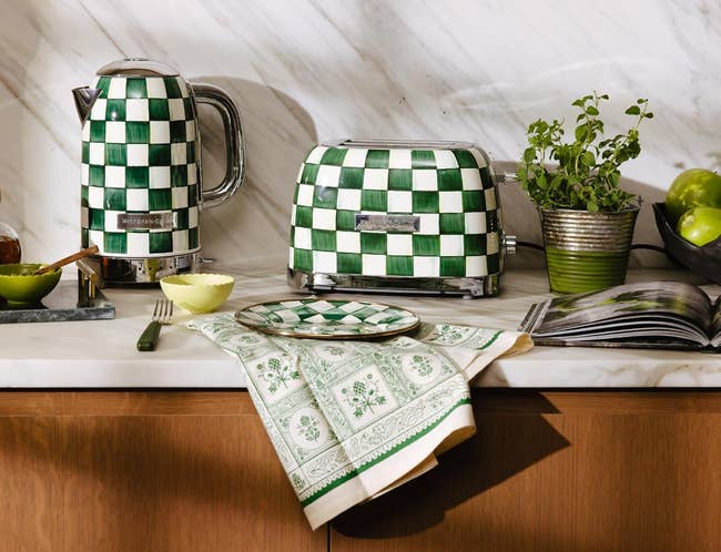 Checkered room appliances with a kettle and toaster connected a countertop, surrounded by plants and a decorative sheet and cloth