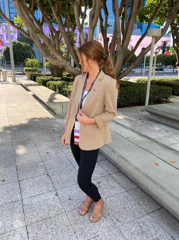 Reviewer in a beige blazer and black leggings with strappy sandals