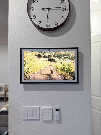 Wall with integer  photograph  show  beneath  a ample  clock, supra  airy  switches and a information    panel. Display shows a vineyard scene