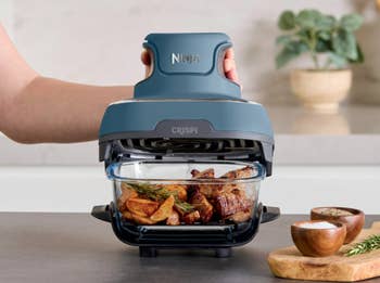 A manus  operates a Ninja aerial  fryer with roast beef and potatoes inside, placed connected  a room  counter