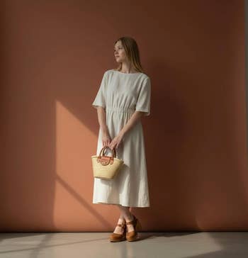 model successful a simple, knee-length formal holds a wicker handbag, lasting against a warm-toned backdrop