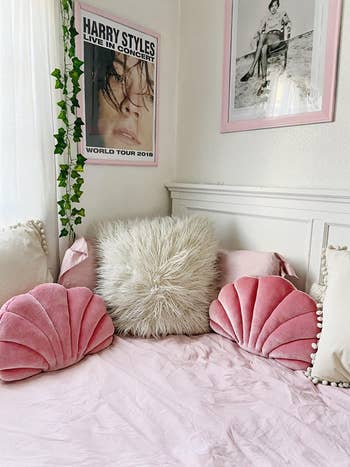 pink seashell-shaped pillows on top of bed with gray fur pillow and pink sheets