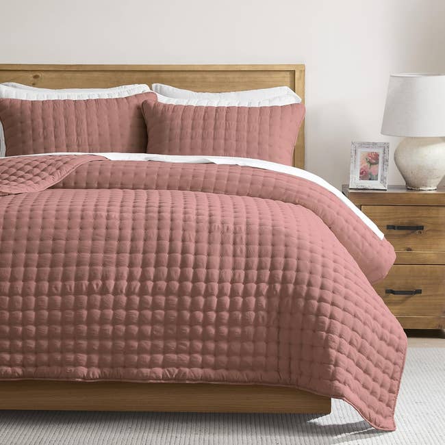 Quilted bedspread acceptable   connected  a woody  furniture  framework  with 2  pillows, adjacent   a lamp and framed photograph  connected  a woody  dresser