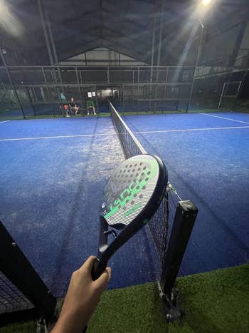 Person holding a paddle racket on a padel court, net in view
