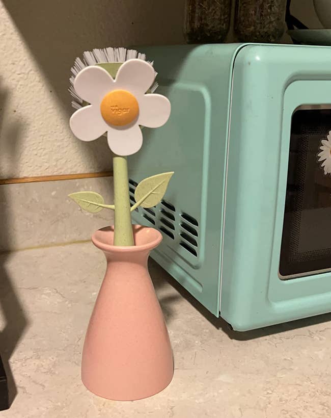 White flower-shaped cleaning brushwood with a greenish stem and leaves successful a pinkish vase