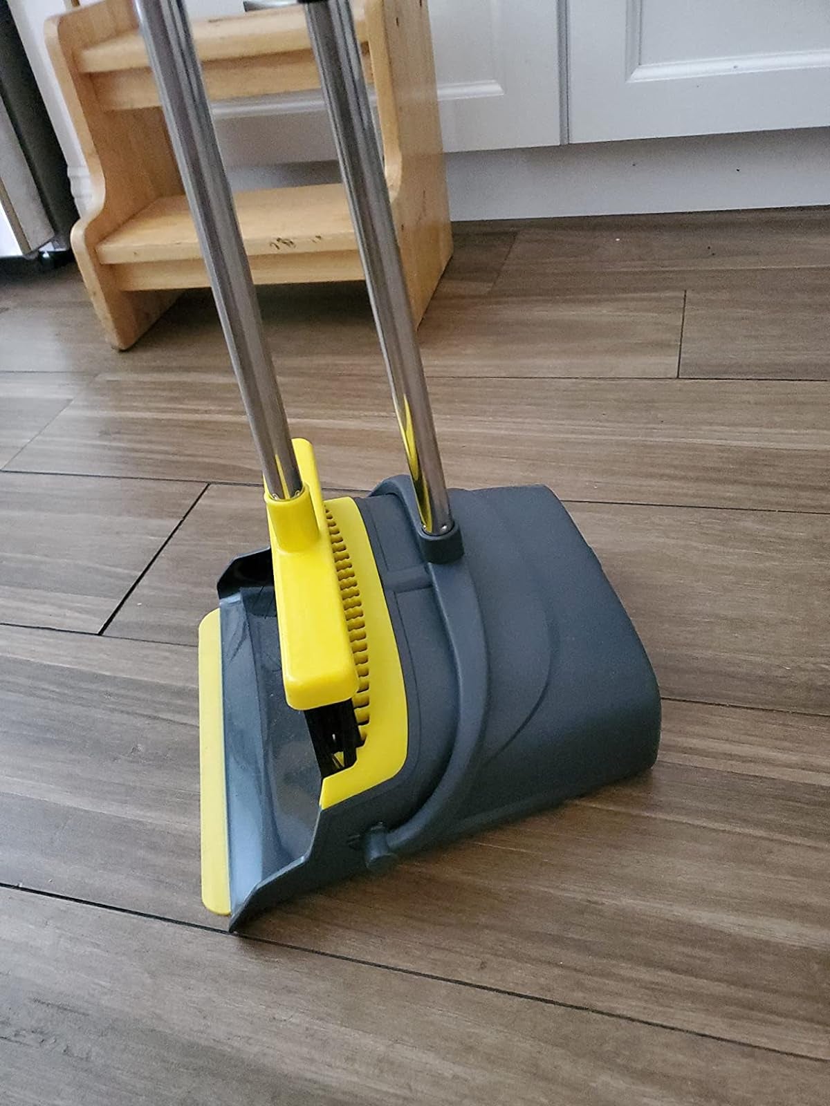 An yellow broom with a gray dustpan with slotted edges to clean the bristles of the broom 