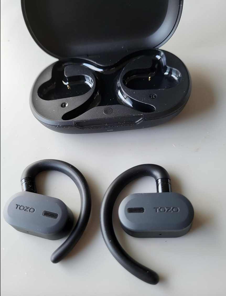 Wireless TOZO earbuds with hooks next to open charging case 