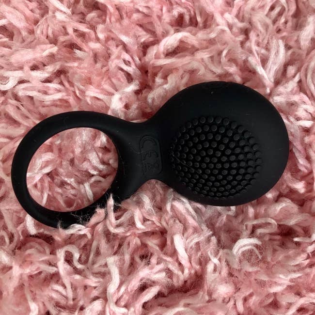 Black cock ring with textured vibrating pad on pink plush rug