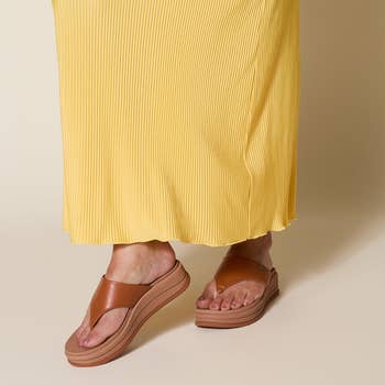 Person wearing pleated skirt and tan level    sandals, showcasing casual, fashionable footwear successful  a buying  context