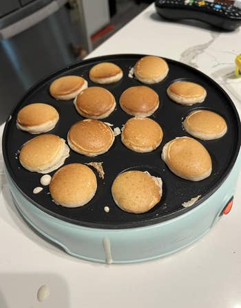 Mini pancakes cooking on a round griddle appliance on a kitchen counter