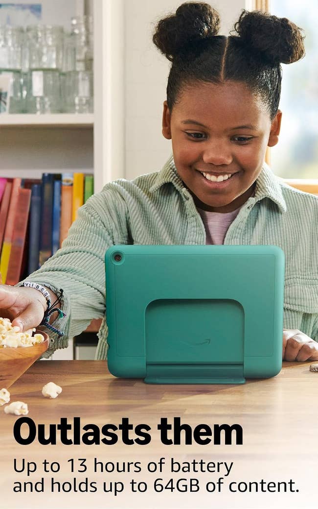 Smiling kid utilizing a tablet with a kickstand astatine a table, reaching for popcorn. Text highlights the tablet's 13-hour artillery and 64GB storage