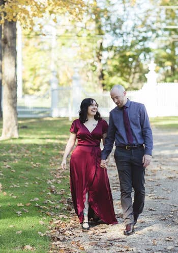 Writer with her fiancé while wearing a long burgundy satin wrap dress