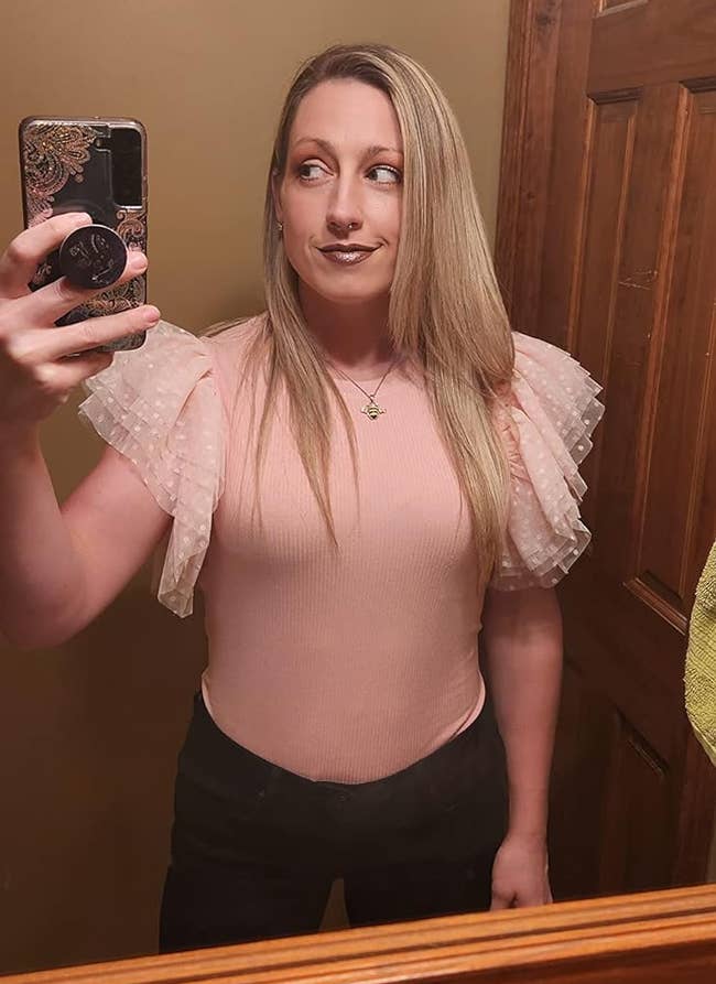 Person takes a mirror selfie wearing a pink top with sheer puffy sleeves and black pants, showcasing a potential outfit