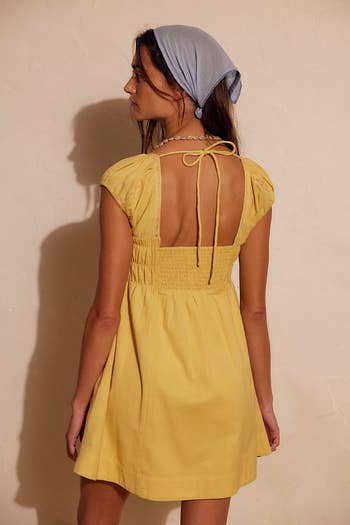 Model in a short dress with smocked waist and open back detail, wearing a headscarf, turned away, showcasing casual summer style