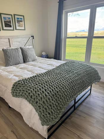 reviewer's neatly made bed featuring a chunky knit blanket draped at the foot