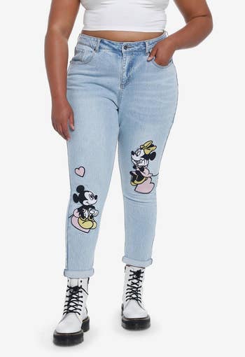 model wearing light wash boyfriend jeans with mickey on one leg and minnie on the other, both sitting on hearts