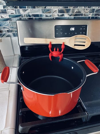reviewer photo of the silicone crab spoon rest holding a wooden spoon and affixed on a red pot