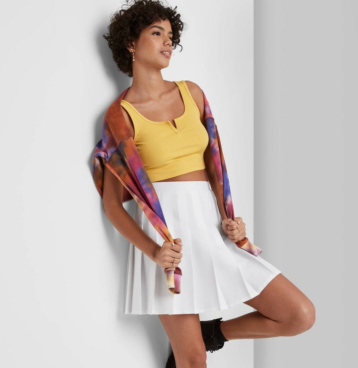 a model wearing a white pleated skirt with a yellow crop top 