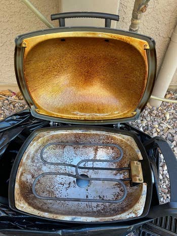 Open portable grill with rusty interior and exposed heating element, acceptable   connected  gravel