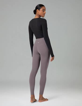 Model poses in fitted activewear, showcasing long-sleeve top and high-waisted leggings. Suitable for workout or casual wear
