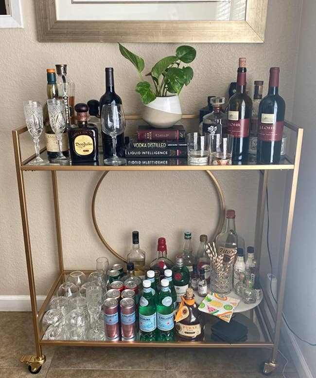 reviewer photo of the gold bar cart stocked with bottles and other bar accessories against a wall