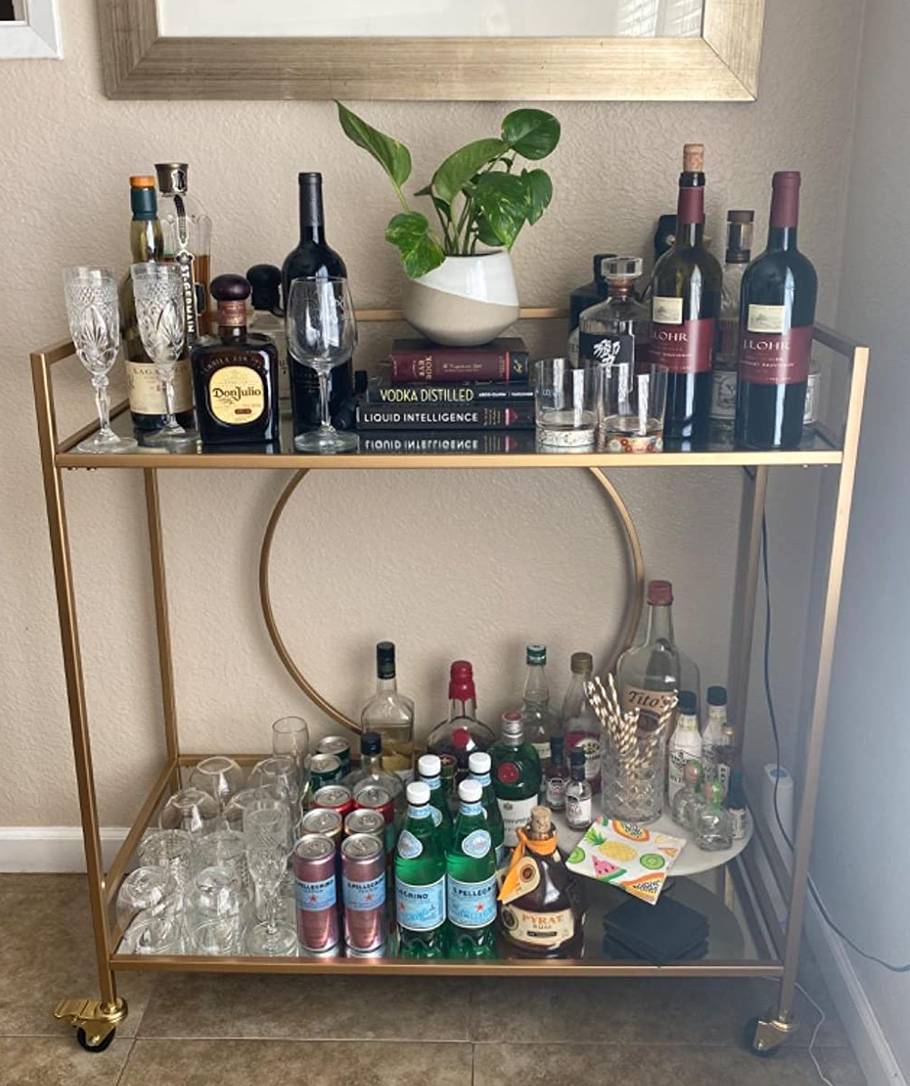 reviewer photo of the gold bar cart stocked with bottles and other bar accessories