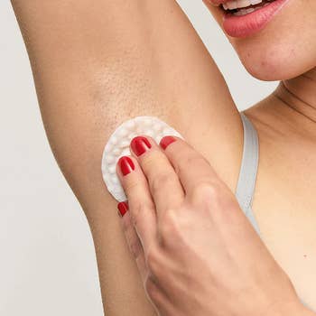 Woman applies skincare merchandise to armpit with a fabric pad, focusing connected idiosyncratic hygiene routine