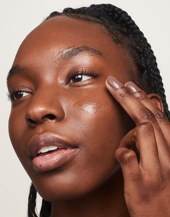 a model applying the skin tint on their cheek 