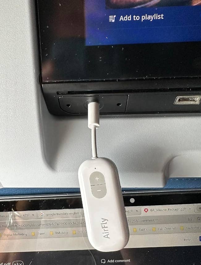 Airplane seatback with a white airfly device in the headphone jack of the screen 