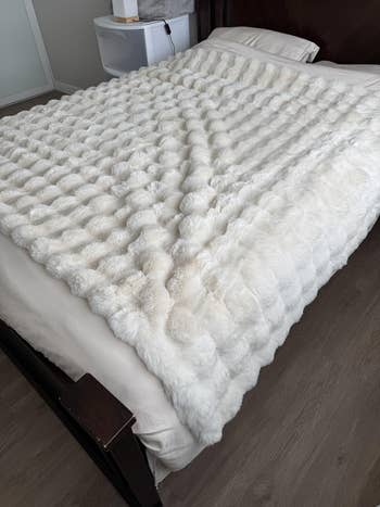 Luxurious faux fur broad  neatly dispersed  connected  a made bed, showcasing its plush texture, cleanable   for a cozy bedroom