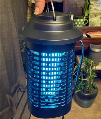 A blue lit up cylinder shaped bug zapper with a handle on top 