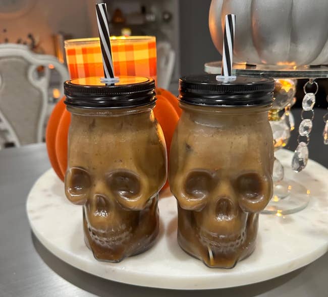 Two skull-shaped mugs with black-and-white straws