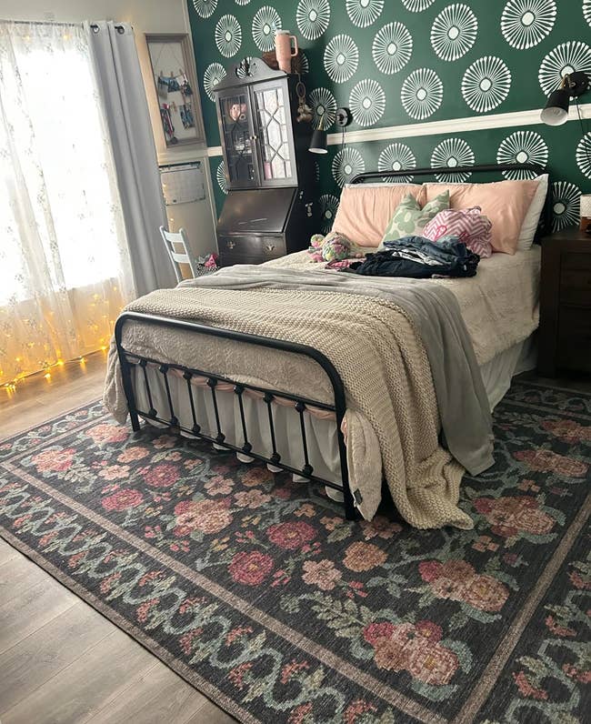 Bedroom with an unmade bed, floral rug, and decorative wallpaper, showcasing a cozy interior design style