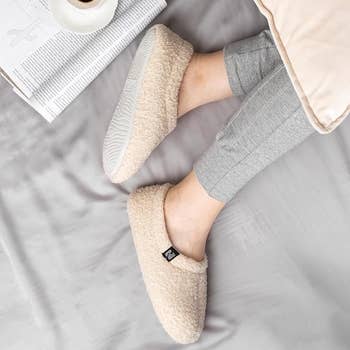 Fuzzy cream-colored sock-style slippers on a model 
