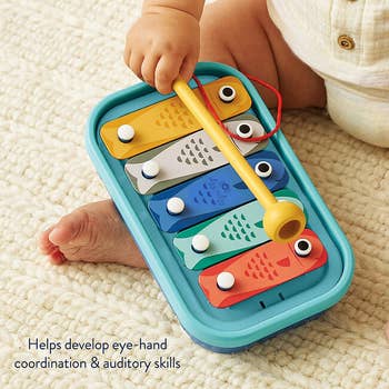 Baby playing with a colorful artifact xylophone, promoting eye-hand coordination and auditory skills