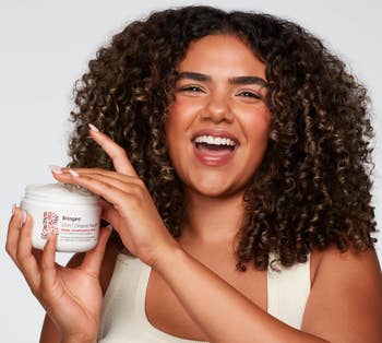 a model holding the open jar of the hair mask
