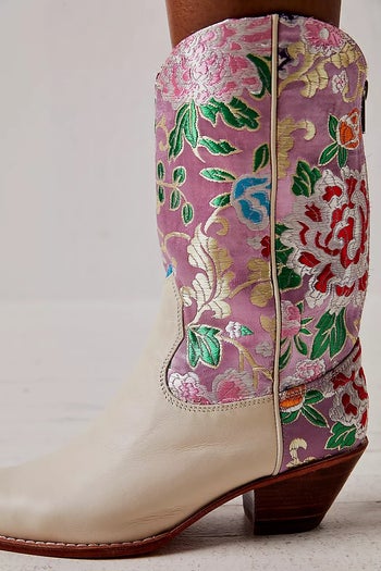A close up of cream boots with pink, silver, green, and gold embroidery