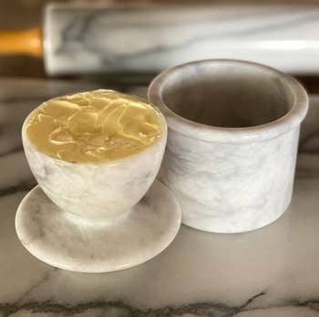 Two marble containers on a countertop one filled with butter and the other with water