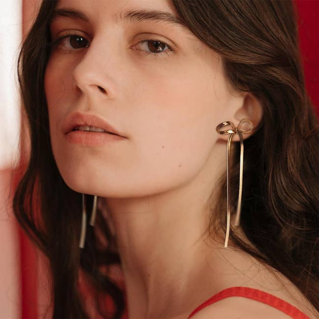 Model in gold bow shaped earrings with long dangling ribbon detail 